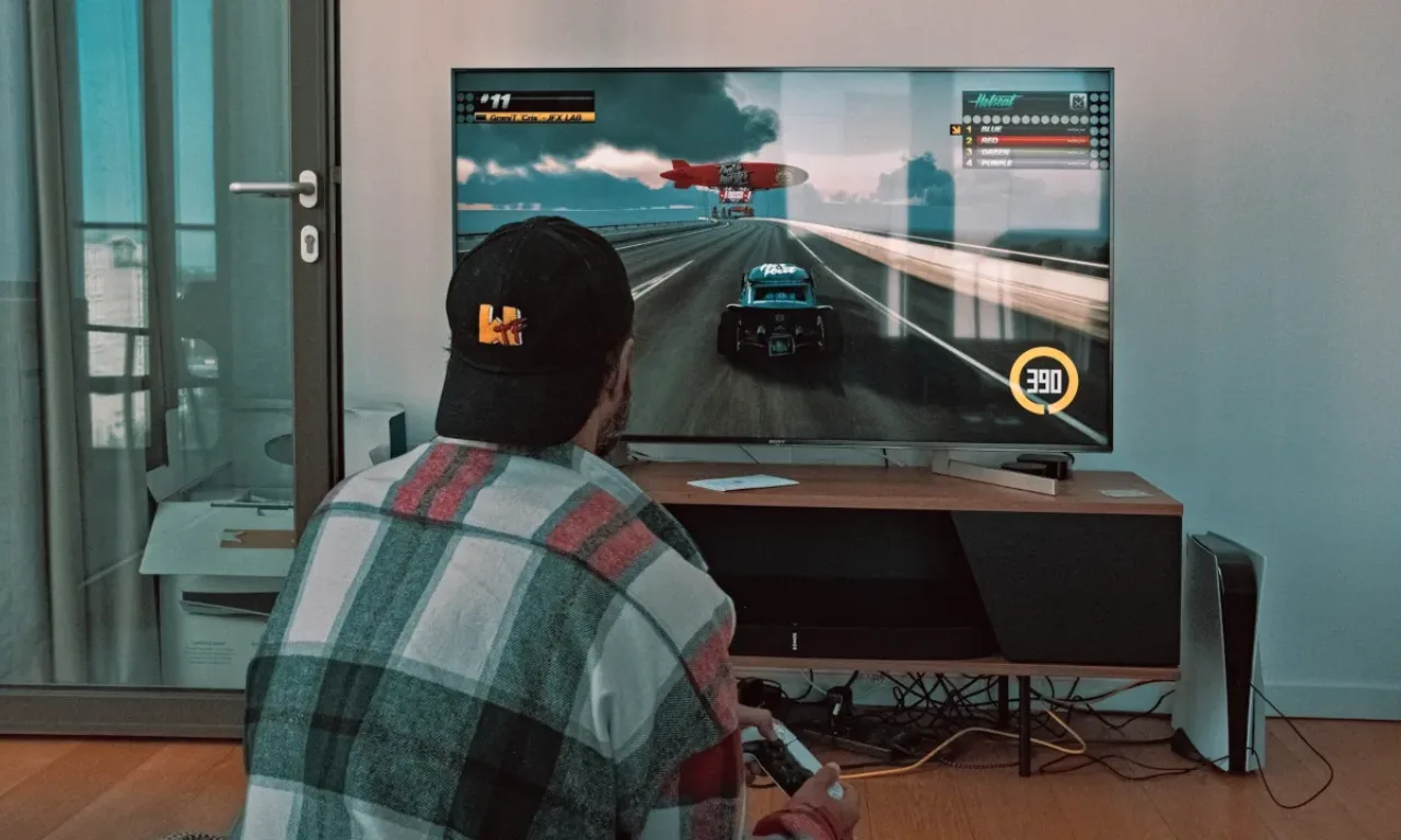 A person playing the racing game with controller in hand and PS5 is standing vertically at the front right.