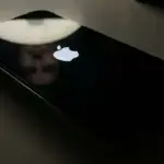 Close-up photograph of an iPhone 14 Pro screen displaying a stuck Apple logo on a black background.